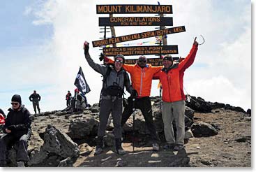 Climbers celebrate in front of the new summit sign on Kili