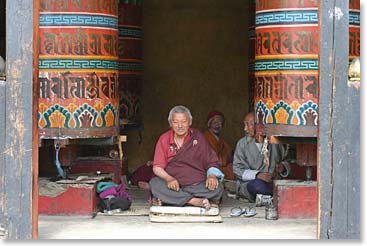 A happy monk rests between giant prayer wheels