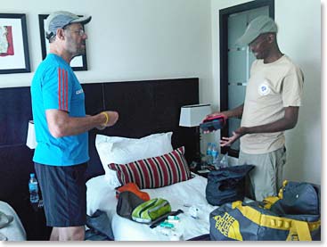 Com ajuda do John, seu guia no Kilimanjaro, checaram o equipamento para a expedição (With the help of John, his Kilimanjaro guide, they went through his gear for the expedition)